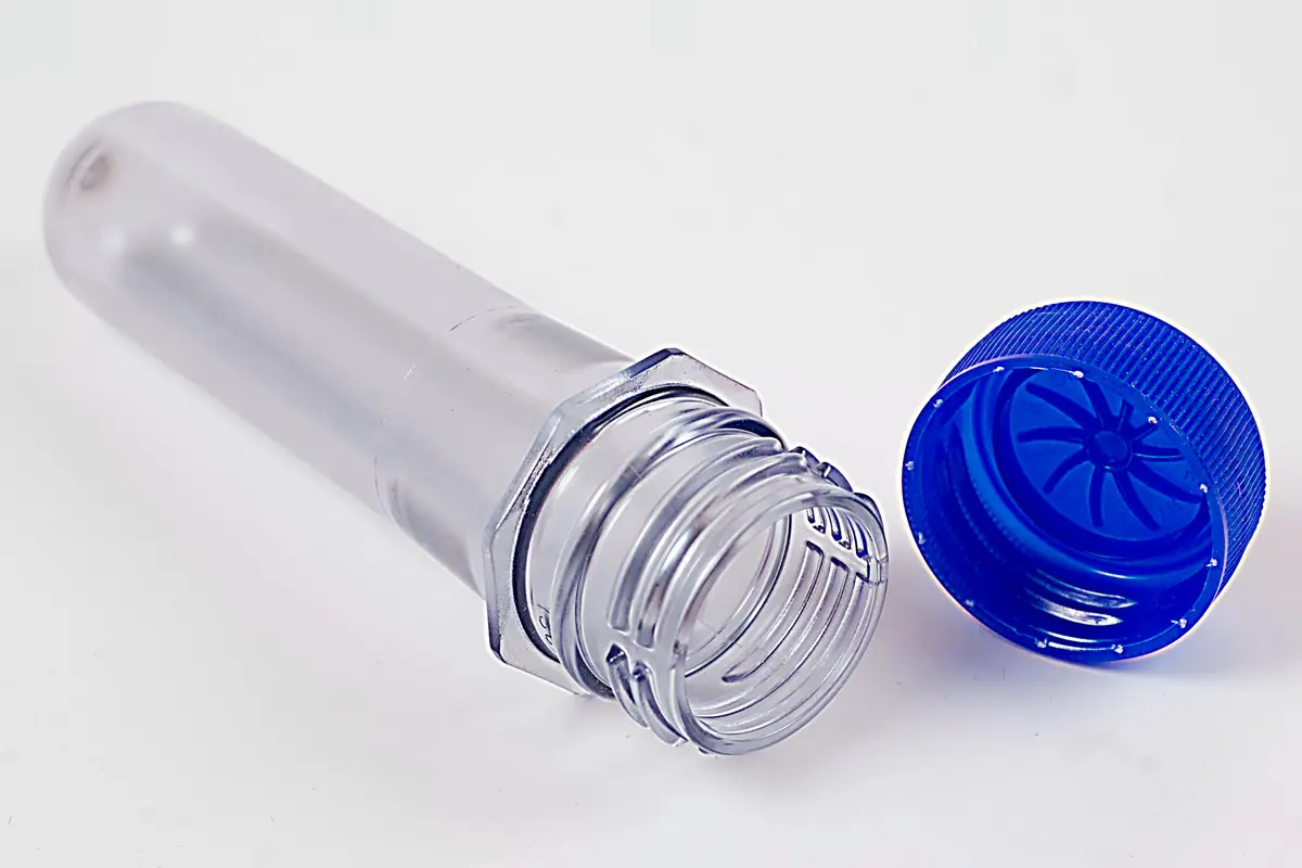 Clear PET preform with threaded neck finish beside a blue closure